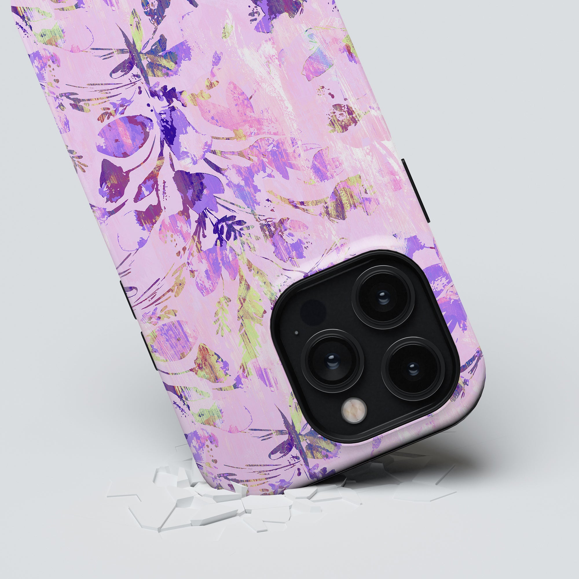 A smartphone with a Spring - Tough Case lying on its side with its camera lenses prominently displayed, against a grey background with some broken pieces beneath it.
