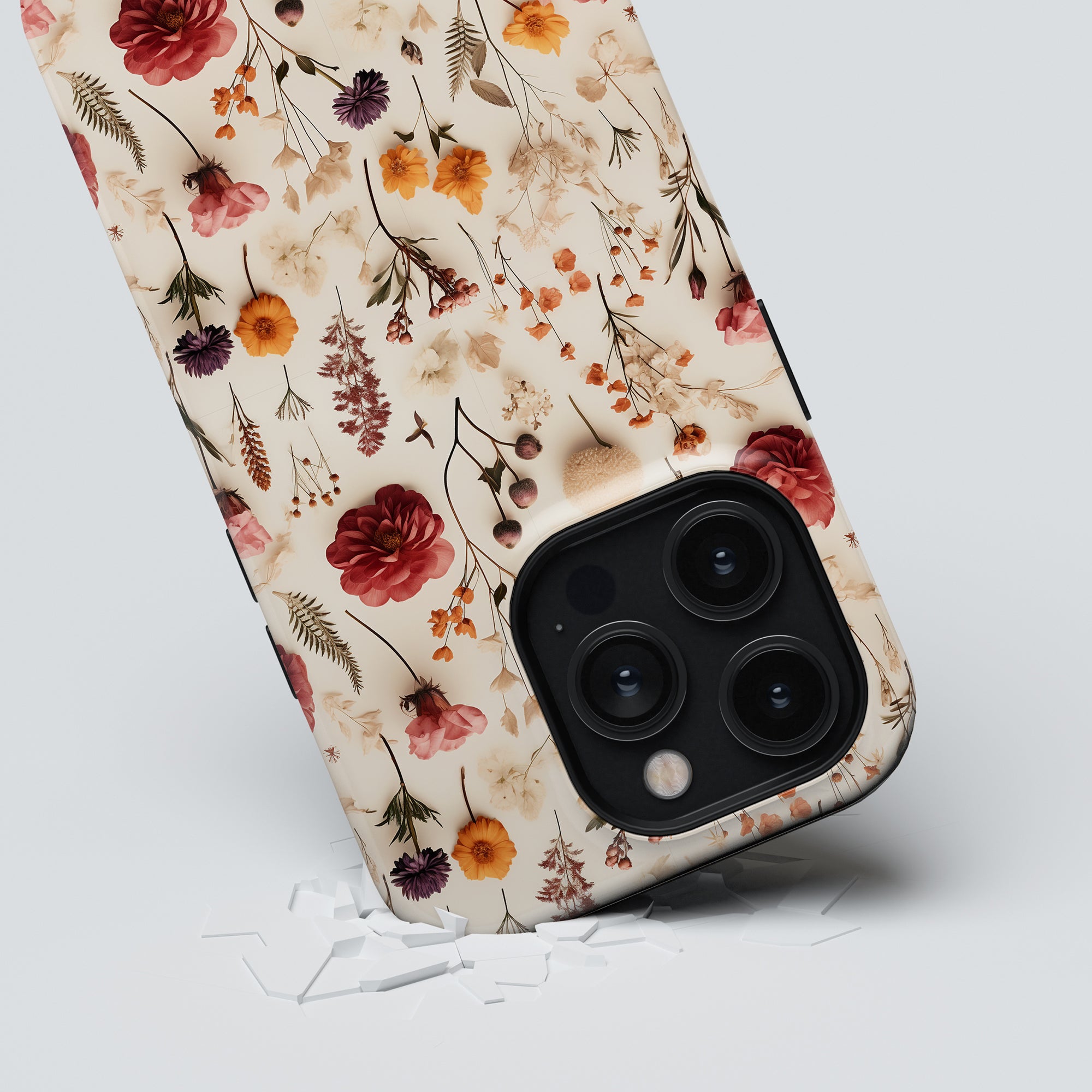 A "Dried Flowers - Tough Case" smartphone case, positioned upright on a plain surface with scattered white fragments around it. Part of the höstkollektion, the phone's camera lenses are clearly visible amidst delicate dried flowers adorning the tough case.