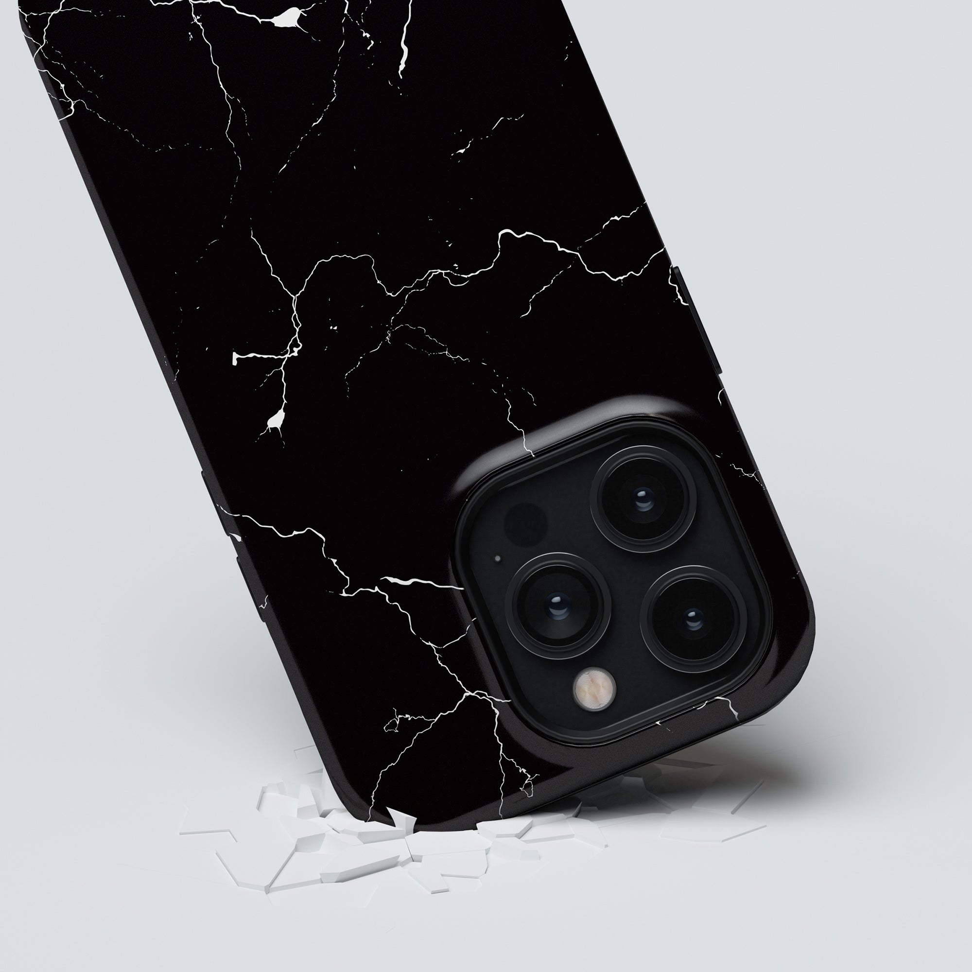 A black smartphone with a cracked screen is leaning on a white surface amidst pieces of shattered glass, clearly in need of the Night Lightning - Tough case for maximalt skydd.