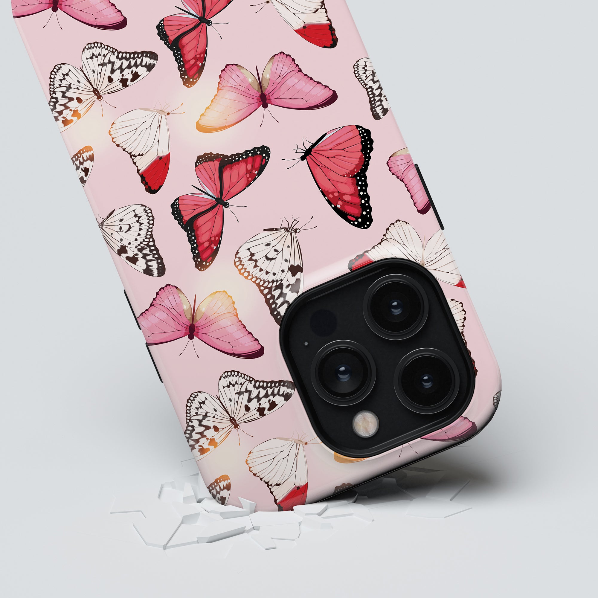 A smartphone with a Rosy Butterflies - Tough case from the Conservatory Collection is positioned against a light background with small white objects scattered below it.