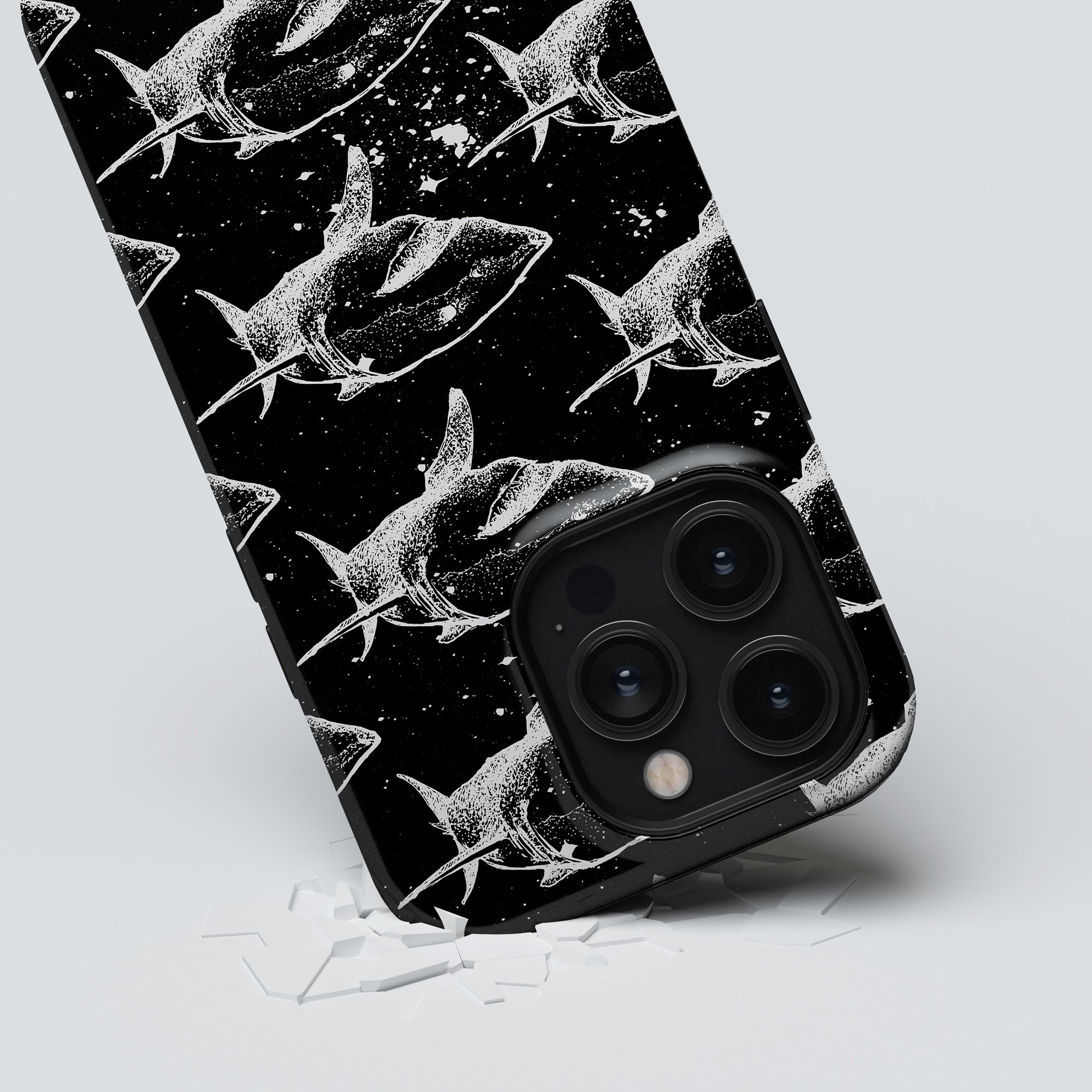 A Shark Attack - Tough case smartphone, featuring a black and white theme, ensuring maximalt skydd, is displayed on a white surface with broken glass pieces strewn around it.