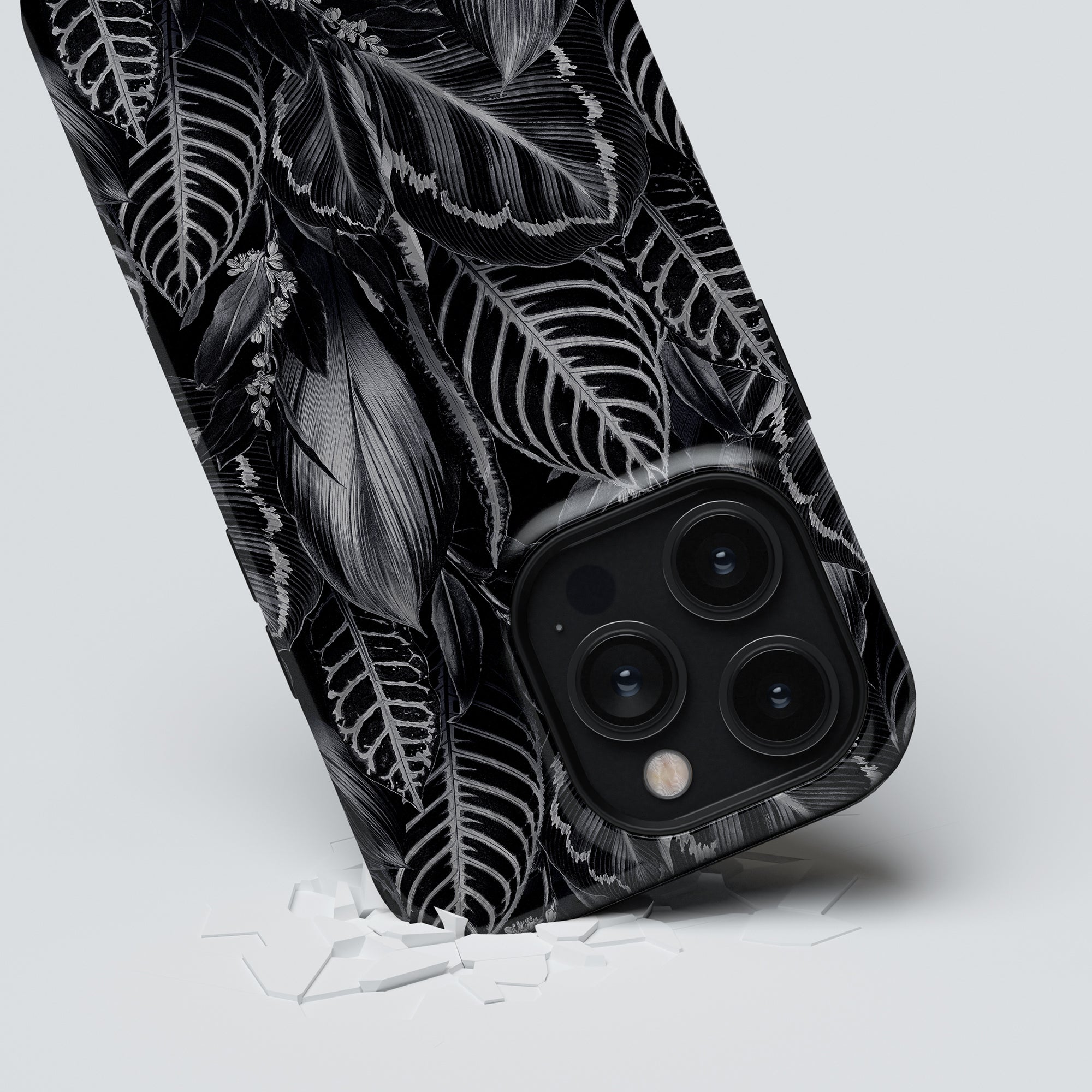 A black smartphone encased in a Dark Leaves - Tough Case with a triple-lens camera protruding through a tear in fabric boasting a leafy jungle collection pattern.